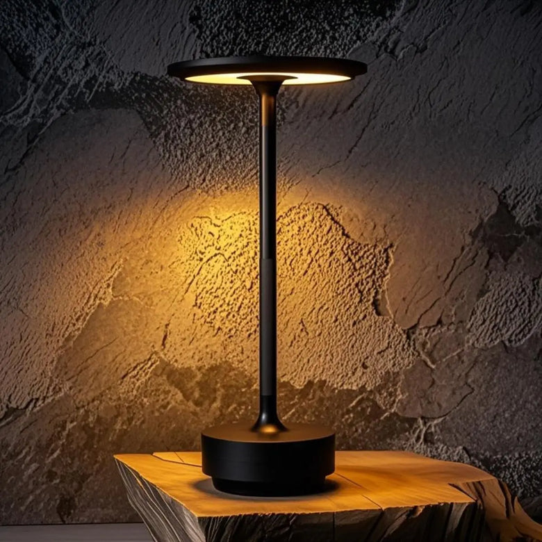 Black Art Deco cordless disc table lamp glowing on a rustic wood slab