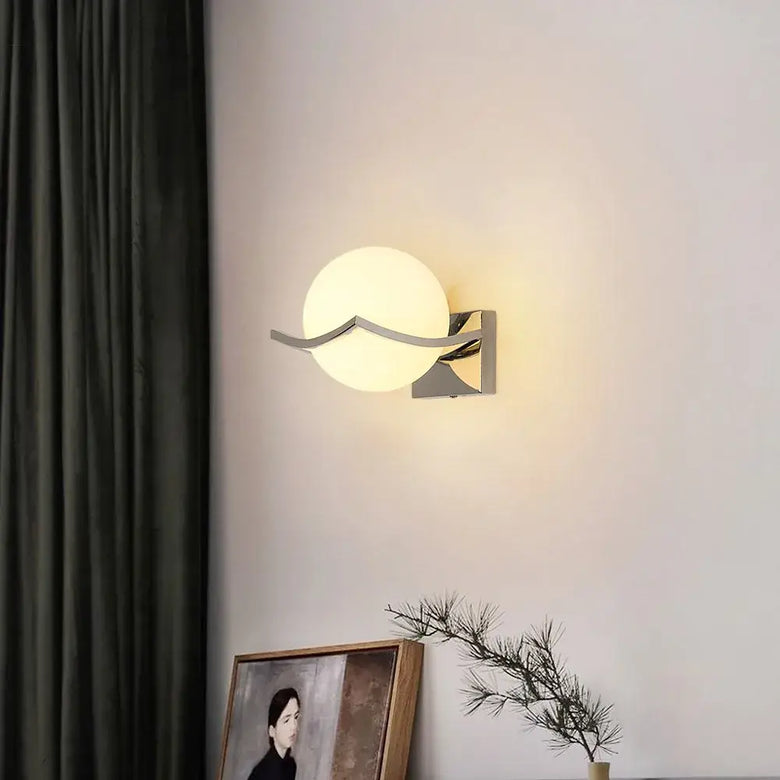 Modern Chrome Wall Sconce with Glass Globe Shade illuminating a wall with a stylish design and warm glow.