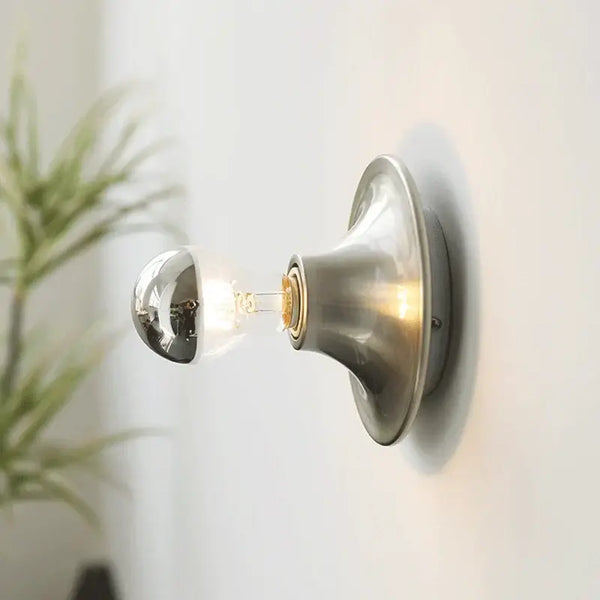 80s revival wall light featuring a stylish UFO shape with a silver top and exposed bulb on a wall.