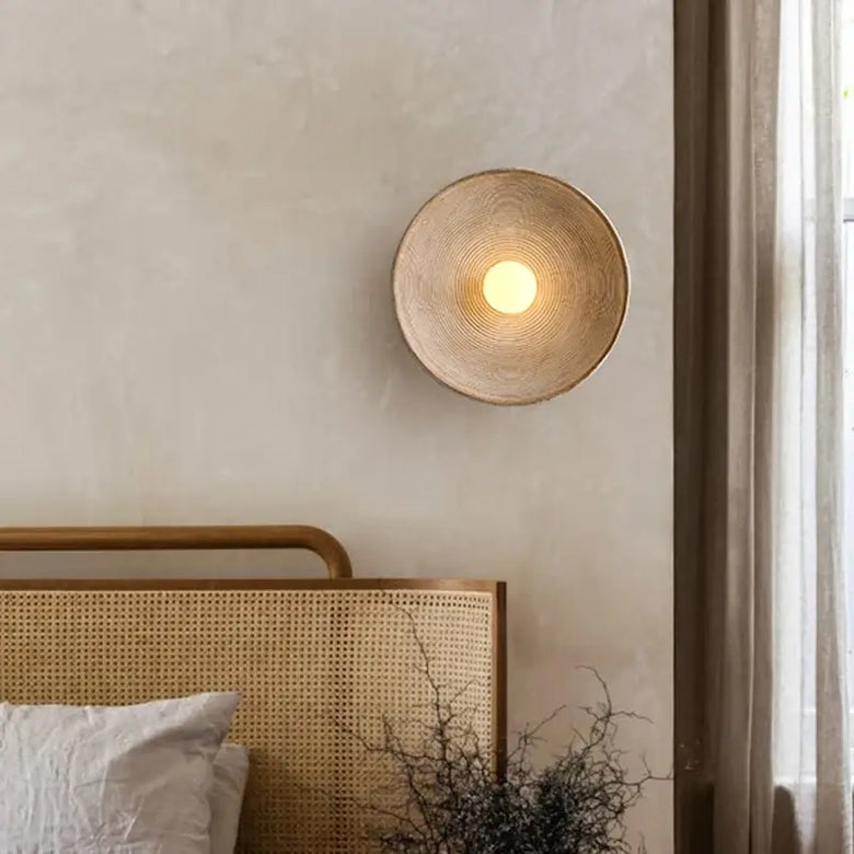 hero Woven wall lamp on a neutral wall above a bed with a wooden headboard.