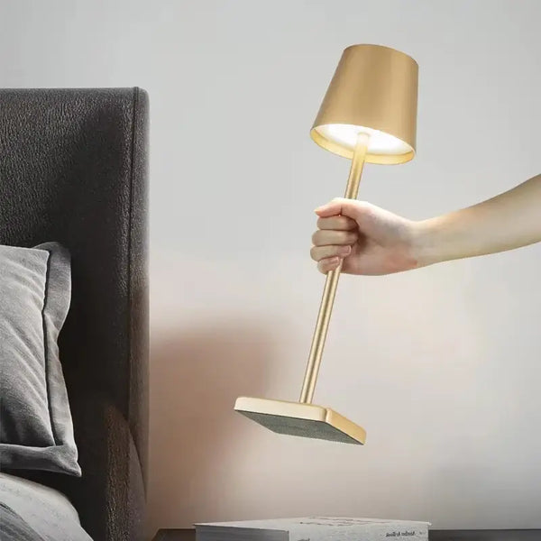 LED Rechargeable Modern Touch Desk Lamp being held next to a bed with soft lighting.