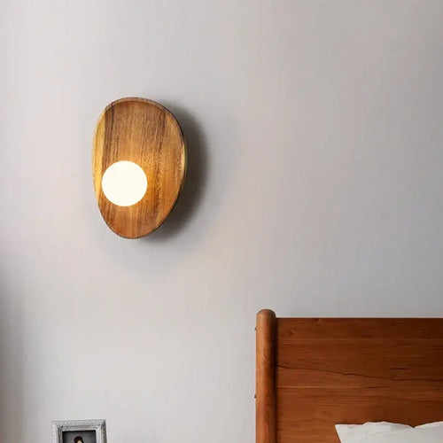 Vintage Walnut Wall Light mounted on a wall beside a wooden bed, showcasing its unique design and warm glow.
