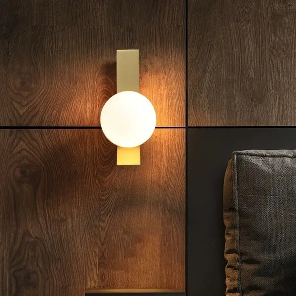 Contemporary Golden Wall Lamp with Glass Ball illuminating a wooden wall backdrop.