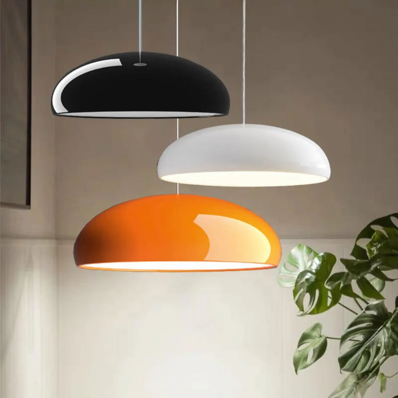 hero - Three pendant lights in black, white, and orange hanging against a neutral background with a plant.
