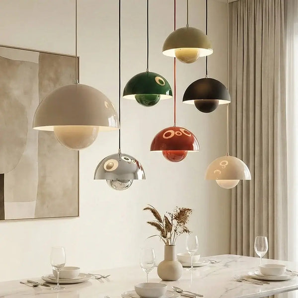Hero A set of seven modern pendant lights with glossy, dome-shaped shades in various colors including beige, green, black, red, and silver, hanging over a styled dining table in a neutral-toned room.