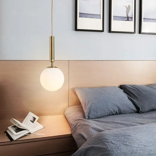 Modern Gold Glass Ball Pendant illuminating a stylish bedroom with a white lampshade and minimalist decor.