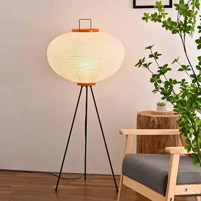 Japanese Rice Paper Lamp. Floor lamp with a round paper shade in a room with a plant and wooden stool.