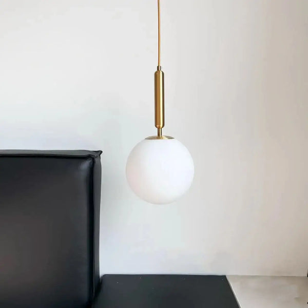 Modern Gold Glass Ball Pendant hanging above a black leather couch in a minimalist interior.