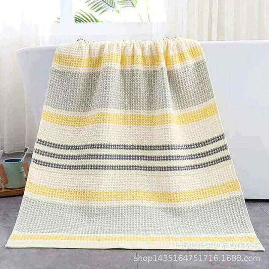 Yellow and gray striped Turkish Towels hanging over a bathtub in a bright bathroom