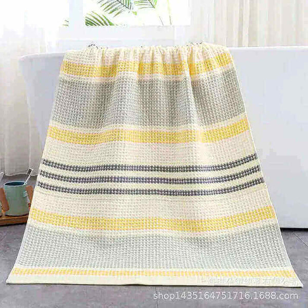 Yellow and gray striped Turkish Towels draped over a bathtub in a bright bathroom setting.