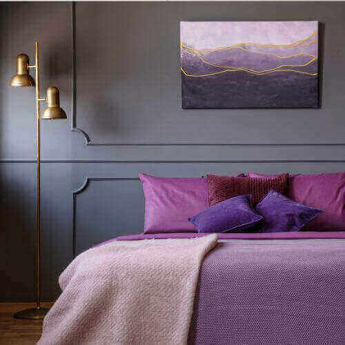 Elegant bedroom showcasing the use of purple in interior design with purple bedding, artwork, and gold accents.