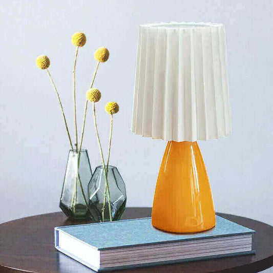 A guide to night stand lamps: Stylish orange nightstand lamp with pleated shade on a book, adding charm to a bedroom.