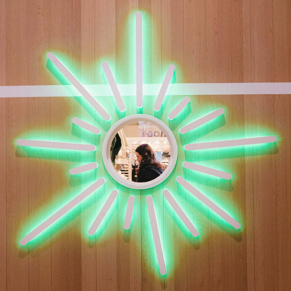 Woman reflected in a sunburst mirror with green lights