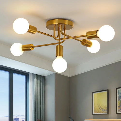 Gold 5-Light Sputnik Ceiling Light with a brushed gold metal frame and spherical glass bulbs, shown installed on a white ceiling in a contemporary room with gray walls and a window.