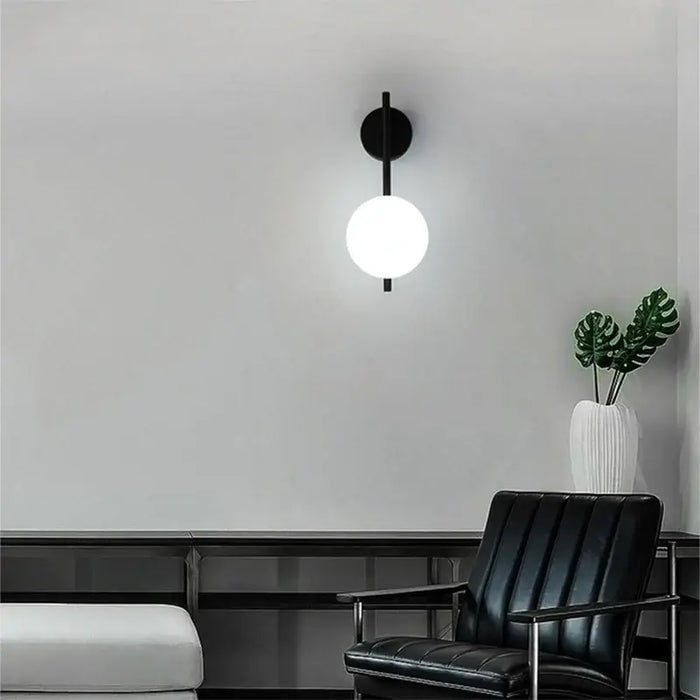Art Deco Golden Circle Sconce illuminating a modern living room with black chair and plant.