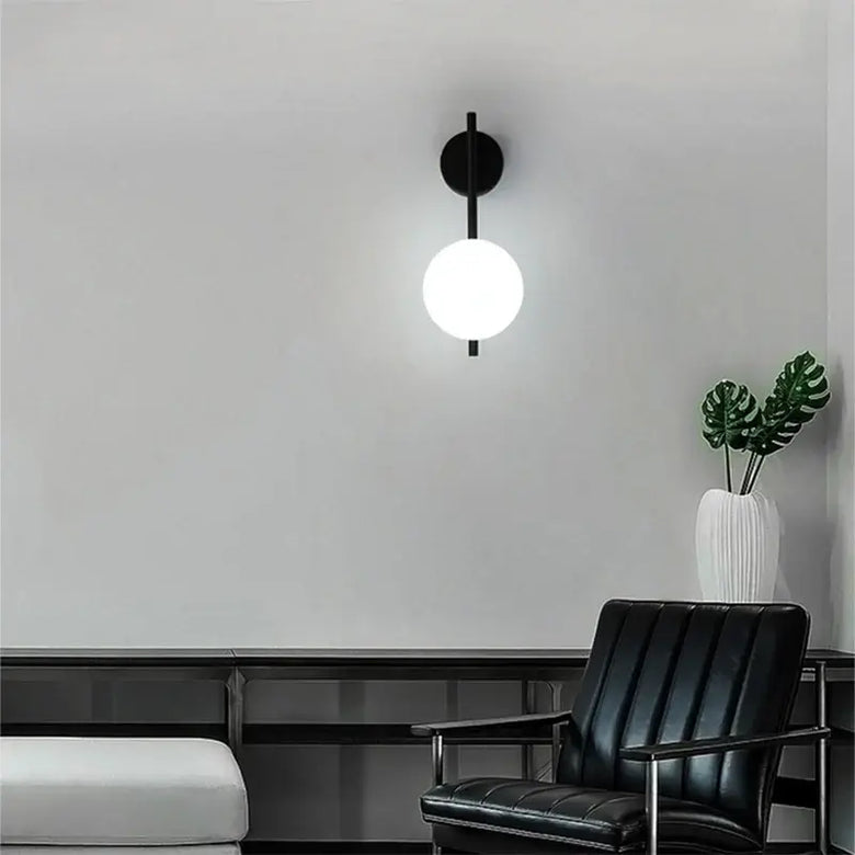 Art Deco Golden Circle Sconce illuminating a modern living room with black chair and plant.