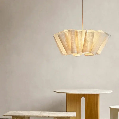 Fabric pleated Chandelier hanging above a minimalist table and bench in a softly lit modern interior.