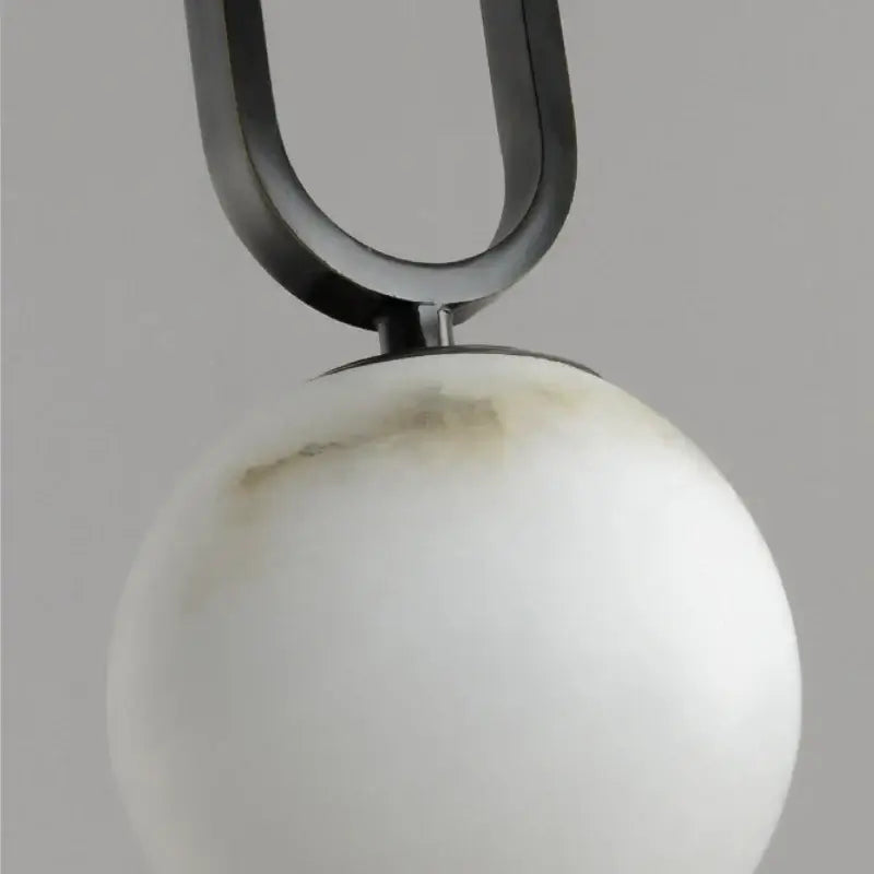Close-up of a pendant with a marble white sphere and black U-shaped metal arm on a gray background