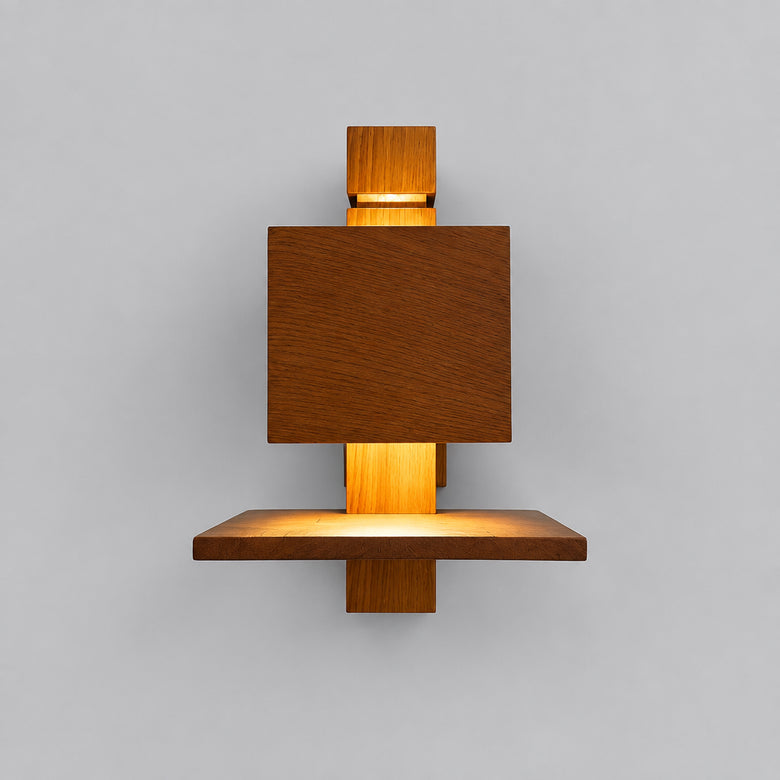 A modern geometric wooden wall sconce with a warm orange light glowing from within, mounted on a plain light gray wall.