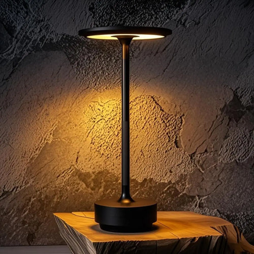 Black Art Deco cordless disc table lamp glowing on a rustic wood slab
