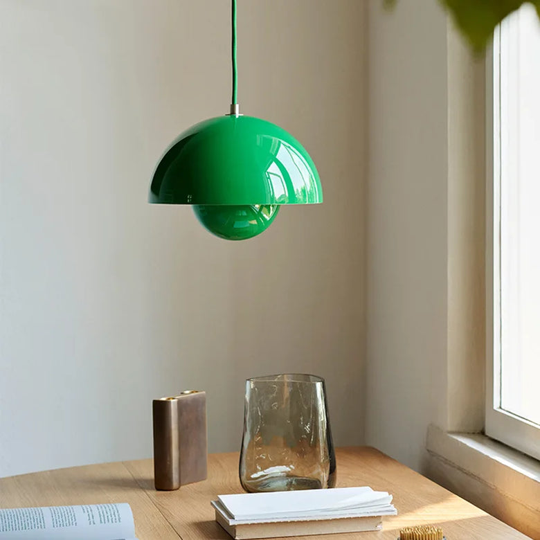Green pendant lamp hanging above a wooden table with a vase and books.