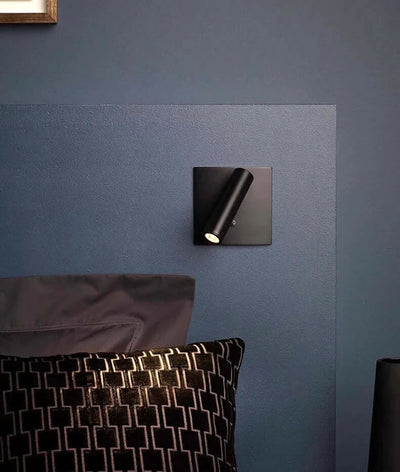 Hero Black wall-mounted light fixture on a blue wall with pillows in the foreground.
