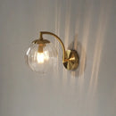 Colourful Glass Modern Wall Light with a golden metal base and transparent bulb on a wall.