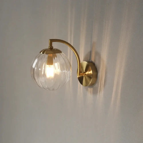 Colourful Glass Modern Wall Light with a golden metal base and transparent bulb on a wall.