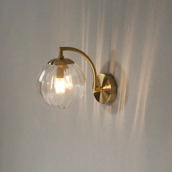 Colourful Glass Modern Wall Light with a golden metal base and transparent bulb on a wall.