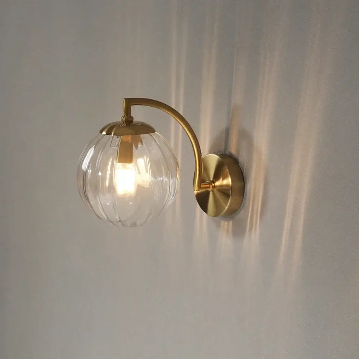 Colourful Glass Modern Wall Light with a golden metal base and transparent bulb on a wall.