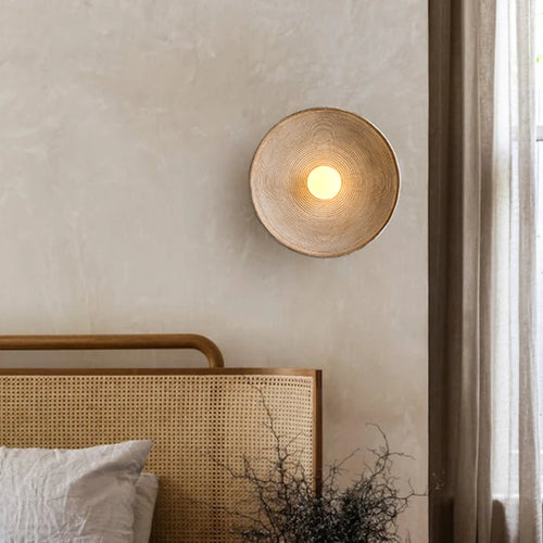 hero Woven wall lamp on a neutral wall above a bed with a wooden headboard.