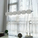 Nordic Art Deco Linear LED Pendant Light – Sculptural Acrylic & Iron Chandelier with white shades by a window.