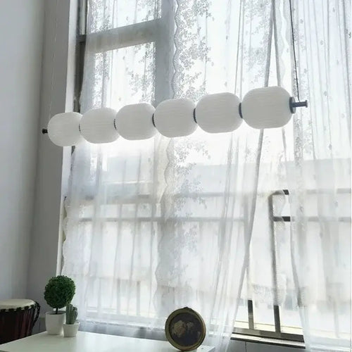 Nordic Art Deco Linear LED Pendant Light – Sculptural Acrylic & Iron Chandelier with white shades by a window.