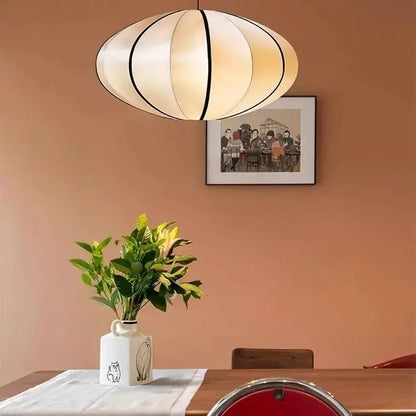Zen Silk Pendant Light Mid Century Fabric Lantern illuminating a dining table with a plant and artwork in a cozy interior.