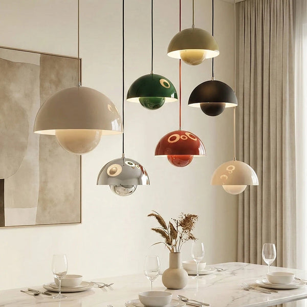Hero A set of seven modern pendant lights with glossy, dome-shaped shades in various colors including beige, green, black, red, and silver, hanging over a styled dining table in a neutral-toned room.