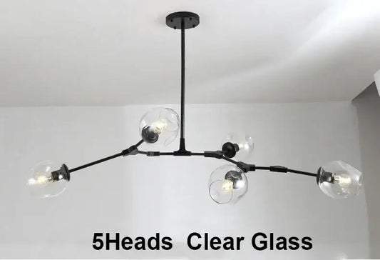 A modern multi-arm ceiling light fixture with a black metal frame and five clear glass globe shades, shown installed against a white ceiling and wall. Text at the bottom reads '5Heads Clear Glass'.