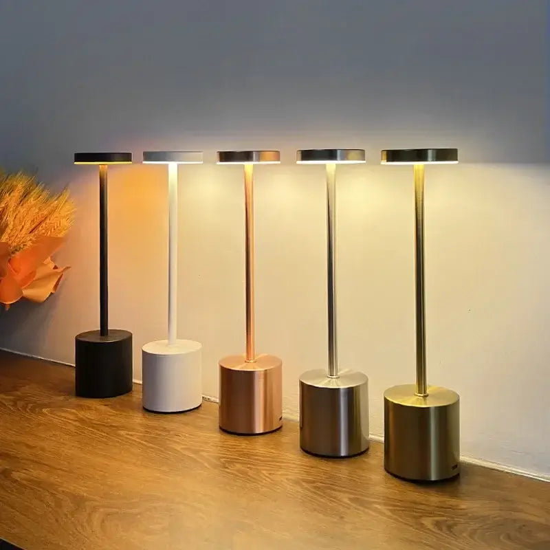 5 modern cordless table lamps with different base colors on a wooden surface.