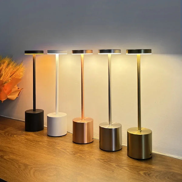 5 modern cordless table lamps with different base colors on a wooden surface.