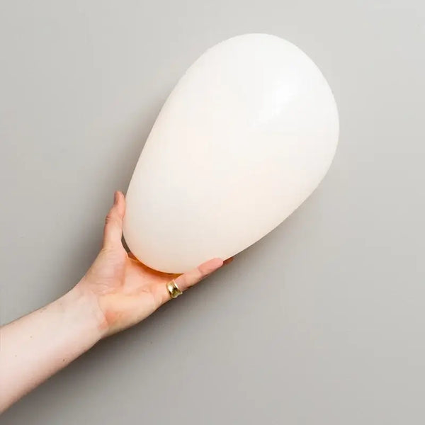 Elegant Frosted Glass Pebble Wall Lamp - Minimalist Nordic Style being held by a person against a neutral wall.