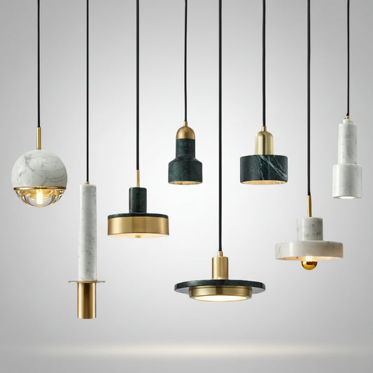 Hero A set of modern pendant lights with black cords, featuring marble and dark green stone cylindrical and spherical shades with gold metal accents, shown against a plain white background.