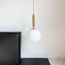 Modern Gold Glass Ball Pendant hanging above a black leather couch in a minimalist interior.