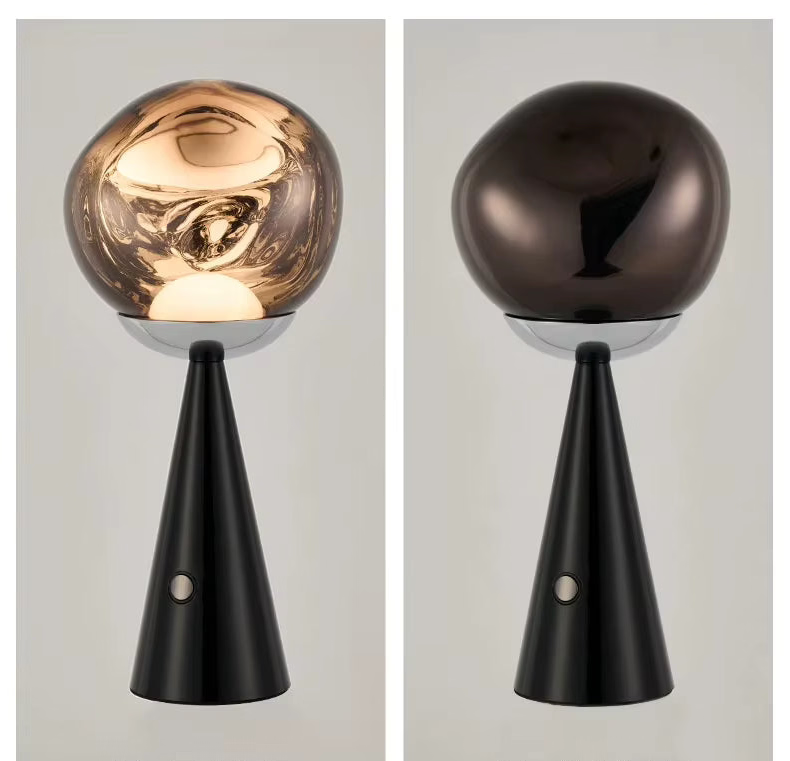 Two modern  Lave Cordless table lamps shown side by side on a light gray background, each with a glossy spherical top and a slim tapered black base. The left lamp has a warm metallic gold/bronze sphere and is turned on, casting a warm glow.