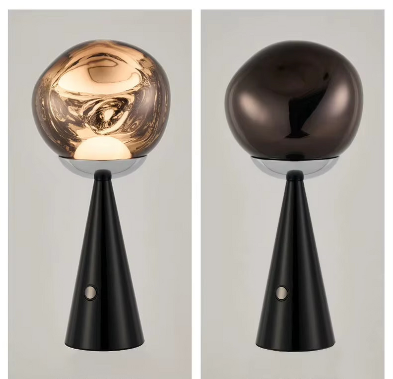 Two modern  Lave Cordless table lamps shown side by side on a light gray background, each with a glossy spherical top and a slim tapered black base. The left lamp has a warm metallic gold/bronze sphere and is turned on, casting a warm glow.