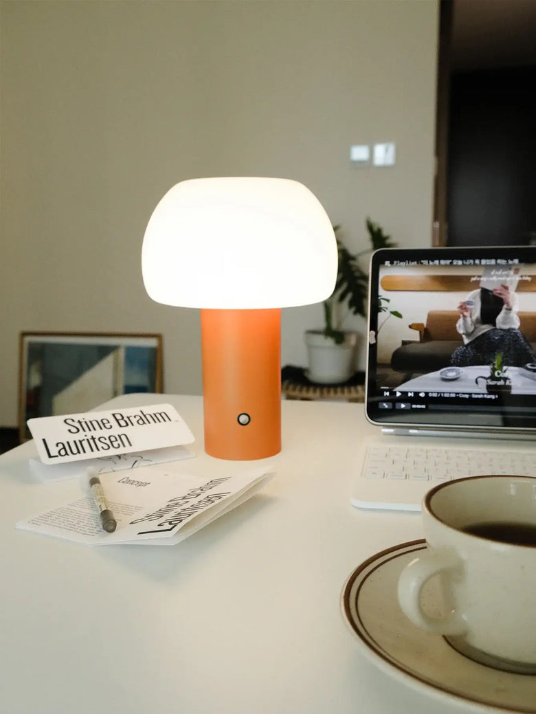Modern Mushroom LED Table Lamp – Rechargeable & Portable Light in orange color on a desk with a laptop and coffee.