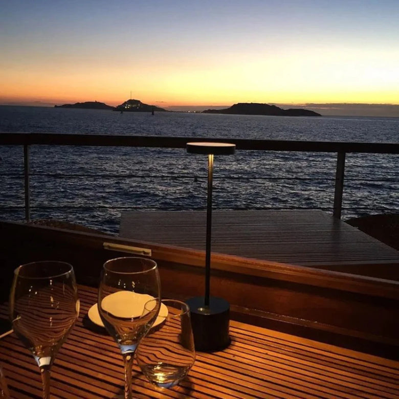 Modern Cordless black lamp on a wooden table with a sunset over the ocean view.