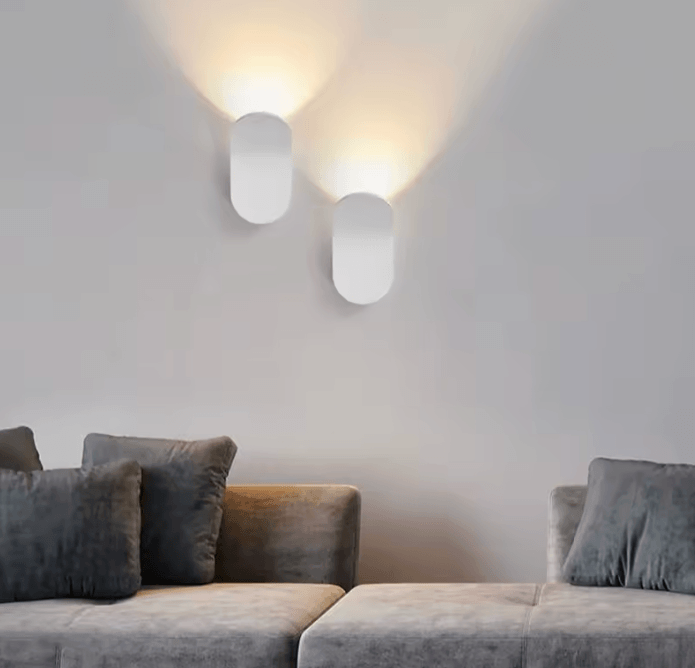 Two modern white japanese wall sconces mounted on a light gray wall above a gray sofa in a minimalist interior setting.