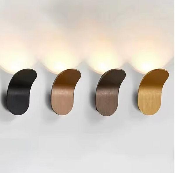 Hero our curved wall-mounted light fixtures in black, bronze, brown, and gold finishes, shown lit against a white wall.