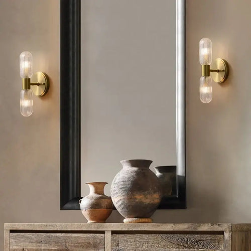 Radiant Luxe Gold Wall Sconce illuminating a stylish interior with decorative vases and a modern mirror.