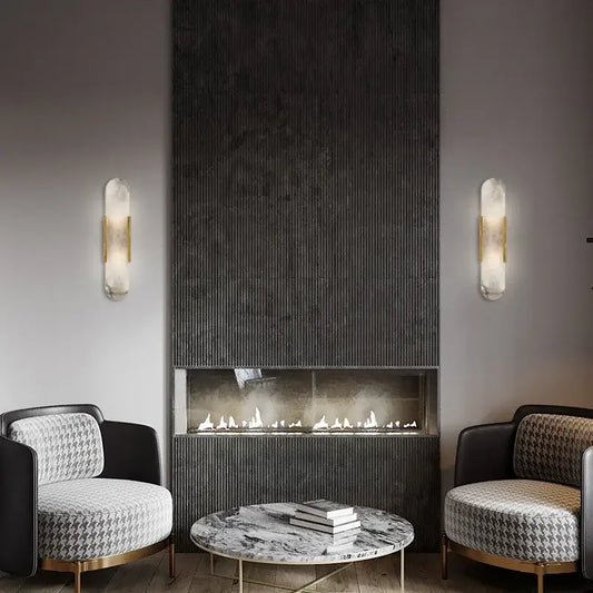 Posh Marble & Gold Roman Villa Sconce illuminating a modern living room with stylish chairs and a fireplace.