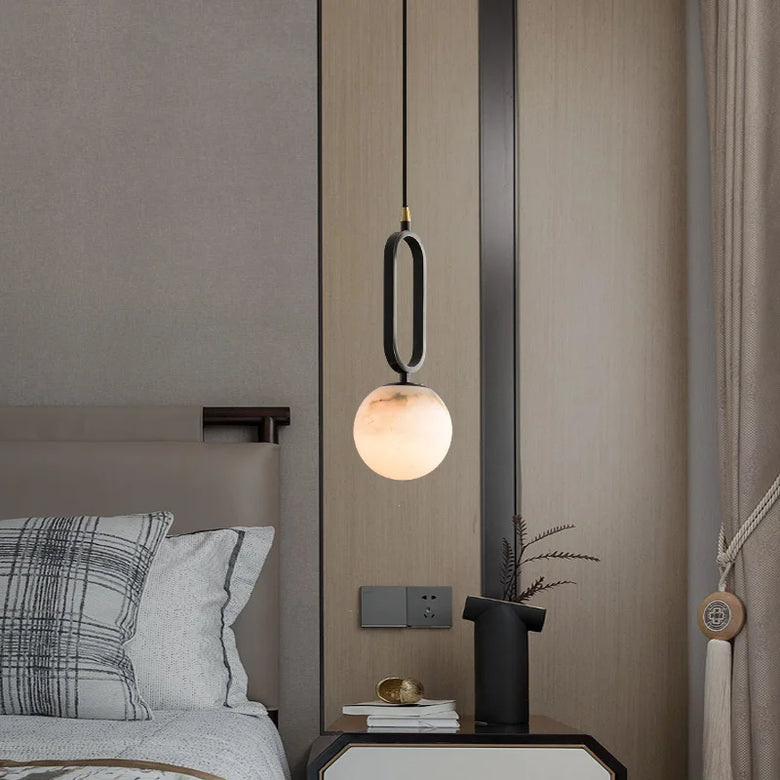 Modern pendant light hanging above a bed in a bedroom setting.